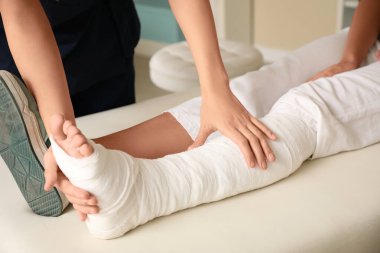Klinikte bacağı kırık bir kadını muayene eden kadın, yakın plan.