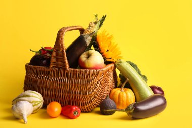 Sarı arka planda taze sebzeler, meyveler ve ayçiçekli hasır sepet. Hasat festivali