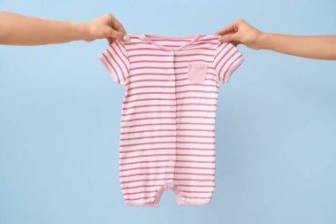 Mavi arka planda bebek tulumu olan kadın elleri.