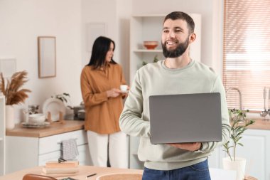 Genç sakallı adam mutfakta dizüstü bilgisayarla çalışıyor.