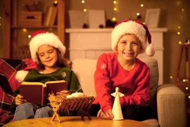 Ahırı ve meleği olan küçük çocuklar akşam evde Noel hikâyesi okuyorlar.
