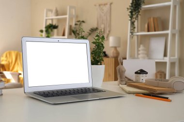 Oturma odasındaki programcının masasında defterleri ve kulaklıkları olan boş bir dizüstü bilgisayar.