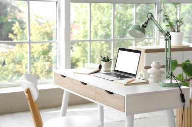 Oturma odasındaki programcının masasında lamba olan boş bir laptop.