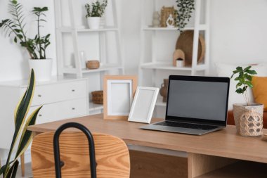 Oturma odasındaki programcının masasında çerçeveleri olan boş bir laptop.