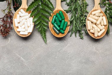 Ahşap kaşıklar dolusu haplar ve arkaplanda bitkiler olan kompozisyon.