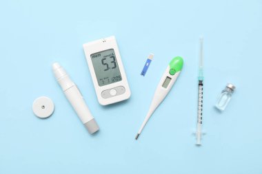 Mavi arka planda glukometre, glikoz sensörü, insülin ve termometre. Diyabet kavramı