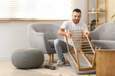 Genç adam evdeki bankta toplanıyor.
