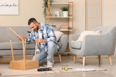 Genç adam evde ahşap masa kuruyor.