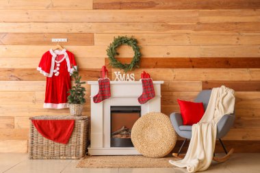 Oturma odasının içinde Noel Baba kostümü, şömine ve Noel çelengi var.