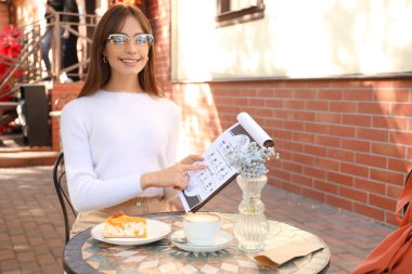 Caddedeki kafede menüsü olan genç bir kadın oturuyor.