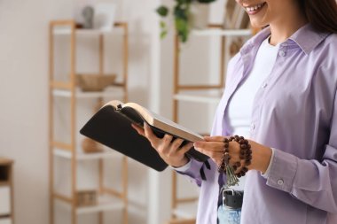 Evinde kutsal kitap ve tespih taşıyan genç bir kadın, yakın plan.