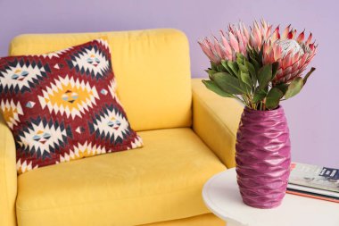 Oturma odasında üzerinde protea çiçekleri ve dergiler olan vazo, yakın plan.