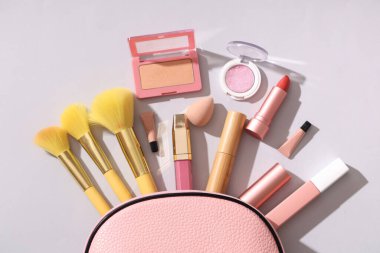 Gri arkaplanda farklı makyaj ürünleri bulunan kozmetik çanta