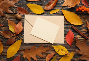 Zarflı kompozisyon, boş kart ve koyu ahşap arka planda düşmüş güzel yapraklar.