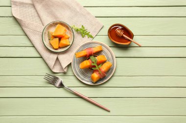 Yeşil ahşap zemin üzerinde prosciutto ve roka ile lezzetli kavun tabağı