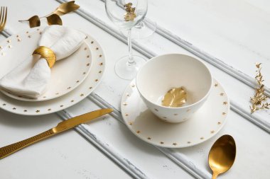 Beyaz ahşap arka planda altın yapraklı ve çatal bıçaklı zarif bir masa.