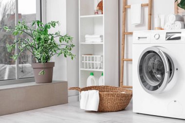 Sepeti, raf ünitesi ve beyaz duvarın yanındaki merdiveni olan modern çamaşır makinesi. Ev çamaşır odasının içi.