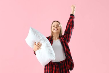 Pembe arka planda yumuşak yastıklı pijamalı genç bir kadın.