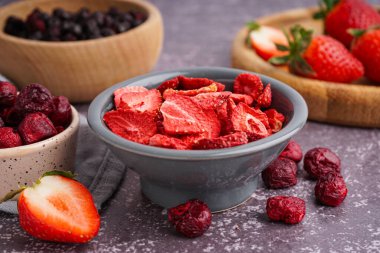 Dondurulmuş çilekli kase ve gri arka planda kirazlar