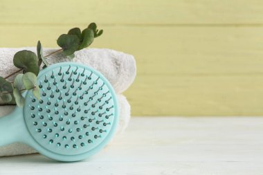 Saç fırçası ve okaliptüs dallı havlular beyaz ahşap masa üzerinde.