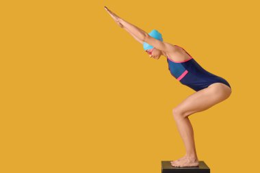 Sarı arka planda, sıçrama tahtasındaki genç bayan yüzücü
