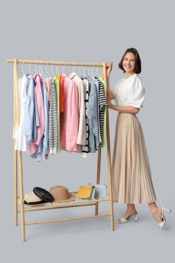 Beyaz arka planda farklı giysileri olan, rafların yanında güzel genç bir kadın.