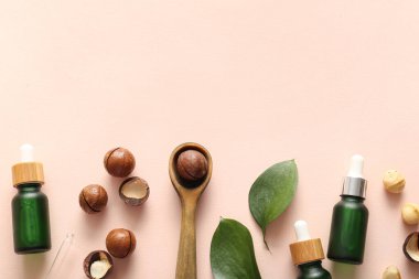 Macadamia fındığı, ahşap kaşık, yeşil yapraklar ve pembe arka planda kozmetik ürünler.