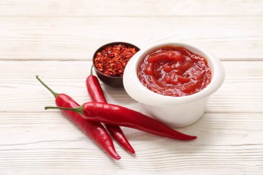 Taze biberli bir kase kırmızı biber ve beyaz ahşap arka planda pullar.