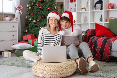 Noel Baba şapkalı mutlu çift, Noel için evde dizüstü bilgisayar alışverişi yapıyor.