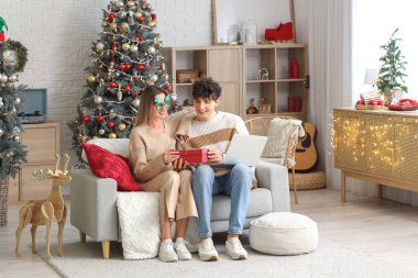 Mutlu genç çift hediye ve dizüstü bilgisayarlarıyla Noel için evde alışveriş yapıyor.