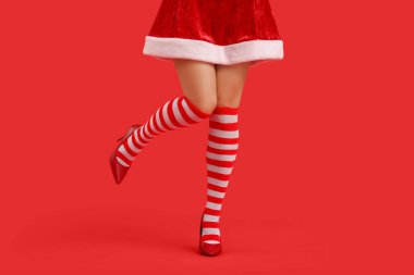 Kırmızı arka planda Noel çoraplı seksi genç kadın bacakları.