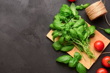 Taze yeşil fesleğen ve siyah arka planda domatesli ahşap tahta.