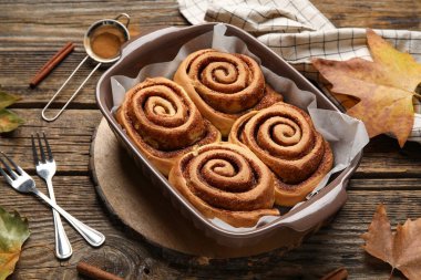 Ahşap zemin üzerinde lezzetli tarçın ruloları ve sonbahar yaprakları pişirme yemeği