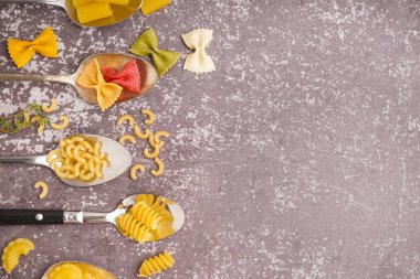 Gri arka planda farklı pişmemiş makarna kaşıkları.