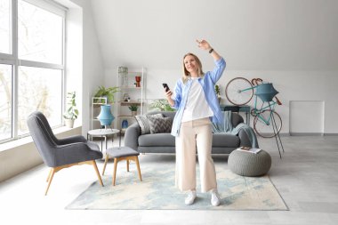 Beyaz oturma odasında cep telefonlu genç bir kadın dans ediyor.