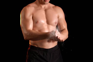 Erkek vücut geliştirici ellerinde pudra sürüyor, koyu arkaplan, yakın plan.