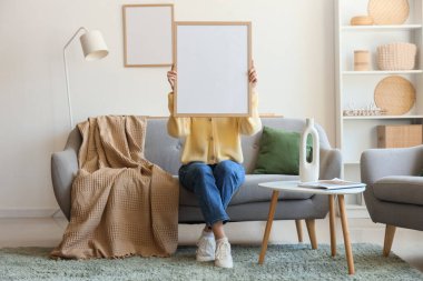 Çerçevenin arkasına saklanan ve oturma odasında kanepede oturan genç bir kadın.