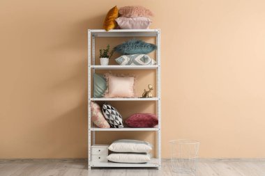 Oturma odasındaki bej duvarın yanında yastıklı ve çiçekli raf ünitesi