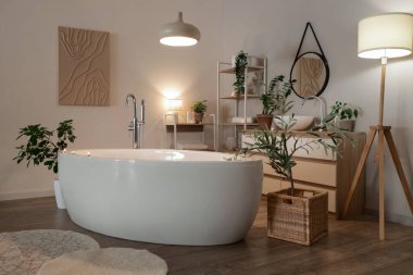 Interior of bathroom with bathtub, plants and glowing lamps at night