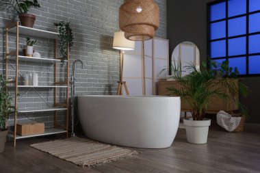 Karanlık banyonun içinde küvet, raf ünitesi ve akşamları parlayan lambalar.