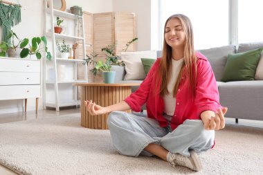 Gülümseyen genç kadın evde halıda meditasyon yapıyor.