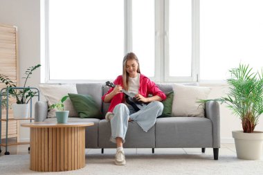 Evdeki kanepede gitar çalan genç bir kadın.