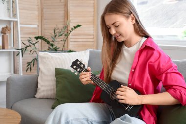 Evdeki kanepede gitar çalan genç bir kadın.