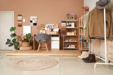 Moda tasarımcısının atölyesinin içinde iş yeri, raf üniteleri ve palmiye ağacı var.