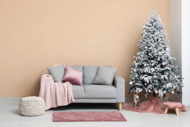 Yastıklı, ekoseli, süslü Noel ağacı ve oturma odasının içinde ren geyiği olan rahat bir kanepe.