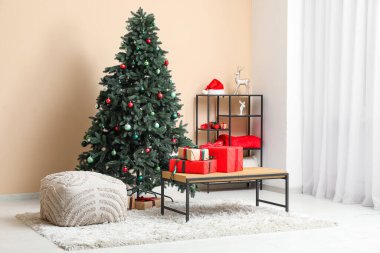 Pouf, hediyeli bank, raf ünitesi ve bej duvarın yanındaki Noel ağacı.