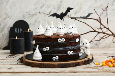 Tatlı Cadılar Bayramı pastası beyaz ahşap masada şekerleme, örümcek ve yanan mumlarla süslenmiş.