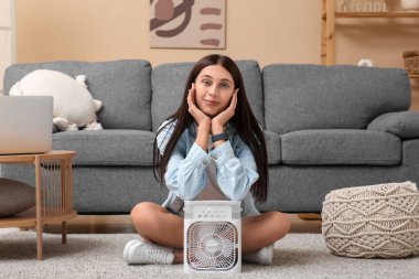 Oturma odasında nemlendirici ile taşınabilir vantilatörün yanında oturan güzel genç bir kadın.