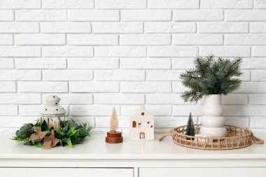 Vazodaki fidan dalları, fener ve beyaz tuğla duvarın yanındaki çekmecelerin üstündeki Noel dekoru.