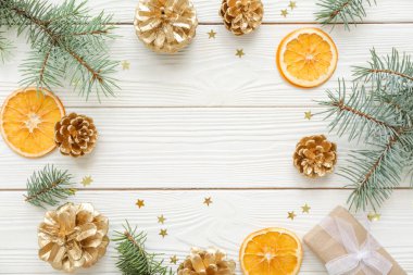 Köknar ağacı dallarından, konilerden, portakal dilimlerinden ve beyaz ahşap arka planda hediyelerden yapılmış çerçeve. Üst görünüm